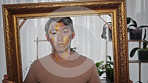 A young Asian man with unusual make-up and a large golden frame posing for the camera.