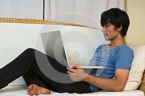 Young Asian man using computeron sofa