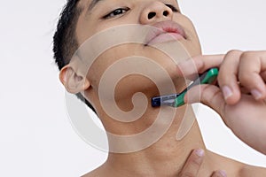 A young asian man using a disposable razor to cleanly shave the beard. Closeup tight shot isolated on a white backdrop photo