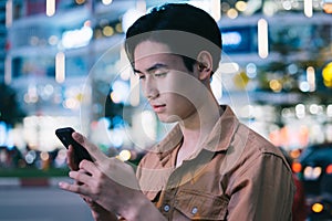 Young asian man is using his phone while walking in the street at night