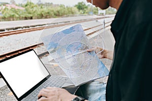 Young asian man using laptop and check map for working and search location for travel at train station. Freelance work and travel