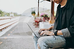 Young asian man using laptop for working and search location for travel at train station. Freelance work and travel concept