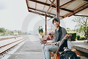 Young asian man using laptop for working and search location for travel at train station. Freelance work and travel concept