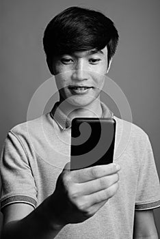 Young Asian man using mobile phone against gray background
