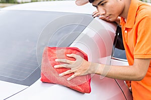 Young man using red microfiber cloth cleaning body of new silver