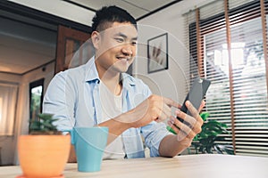 Young Asian man using smartphone while lying on the desk in her living room.
