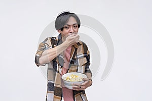 A young asian man voraciously stuffing his mouth with popcorn while watching a movie. Isolated on a white background