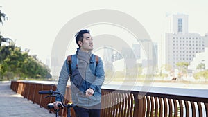 Young asian man walking in city park with bicycle