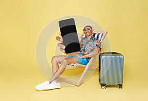 Young asian man wear summer clothes sit in deckchair showing mockup mobile cell phone app booking hotel