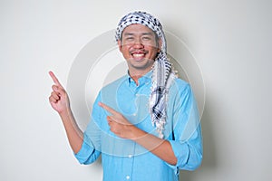 Young Asian man wearing Arabian Shemagh head scarf pointing to his side