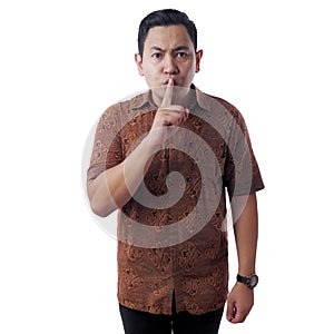 Young Asian Man Wearing Batik Shirt Shows Shushing Gesture