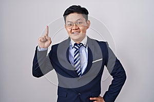 Young asian man wearing business suit and tie pointing finger up with successful idea