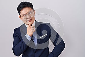 Young asian man wearing business suit and tie thinking worried about a question, concerned and nervous with hand on chin