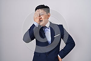 Young asian man wearing business suit and tie yawning tired covering half face, eye and mouth with hand