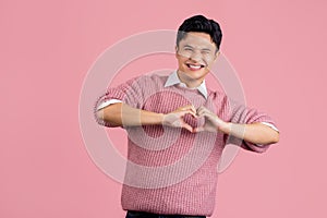 Young asian man wearing casual pink sweater smiling in love doing heart symbol shape with hands. romantic concept