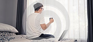 Young Asian man wearing eyes glasses and drinking coffee before working from home with laptop computer. Relaxing shot break after