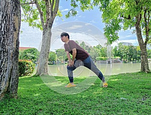 Young Asian man wearing glasses with dark hair standing yoga or warming up under a tree. in the summer park city