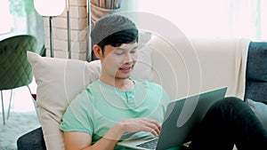 A young Asian man wearing a green shirt, looking down at his laptop computer, and having a serious expression on his work, inside