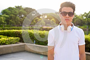 Young Asian man wearing headphones while relaxing at the park