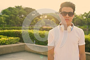 Young Asian man wearing headphones while relaxing at the park