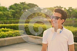 Young Asian man wearing headphones while relaxing at the park