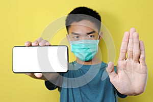 Young Asian man wearing protect mask doing stop gesture to stop share hoax, fake news