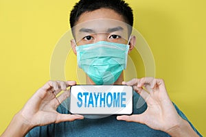 Young Asian man wearing protect mask showing STAYHOME text on phone screen