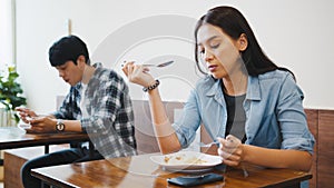Young Asian man and woman having lunch meal in local restaurant, sit in social distance. Business reopening, social distancing