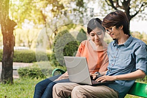 Young asian man and woman working with them laptop on a bench in the park outdoors on vacation time