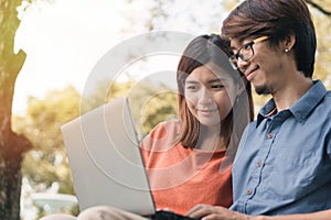 Young asian man and woman working with them laptop on a bench in the park outdoors on vacation time