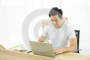 Young asian man working on desk with laptop and mobile phone at sofa at home
