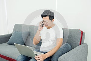 Young asian man working on desk with laptop and mobile phone at sofa at home