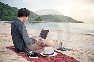 Young Asian man working with laptop on the beach