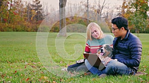 A young Asian man working with a laptop in the park. Near an attractive woman and a dog looking at the monitor