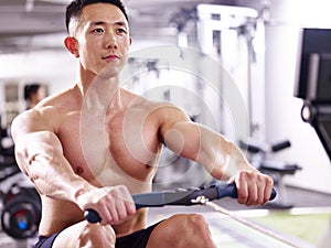 Young asian man working out using rowing machine