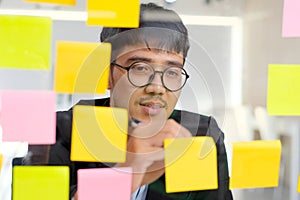 Young asian man writing on sticky note at office, business brainstorming creative ideas, office lifestyle, success in business