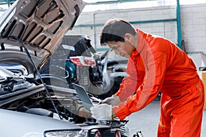 Young Asian mechanic in orange uniform View on laptop about car engine while repairing in garage