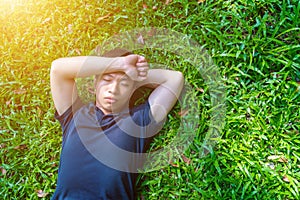 Young asian men lies on green moss relaxing with eyes closed and hands behind his head, feeling comfortable on the grass field