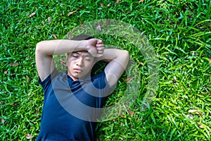 Young asian men lies on green moss relaxing with eyes closed and hands behind his head, feeling comfortable on the grass field