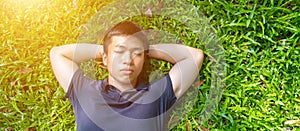 Young asian men lies on green moss relaxing with eyes closed and hands behind his head, feeling comfortable on the grass field