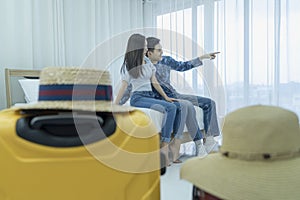 Young Asian man and women are preparing for the journey happily. Young couple relaxing In room looking out of window