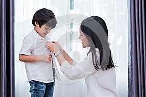 Young Asian mom dressed up son outfits for preparing go to school. Mother and son concept. Happy family and Home sweet home theme