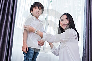 Young Asian mom dressed up son outfits for preparing go to school. Mother and son concept. Happy family and Home sweet home theme