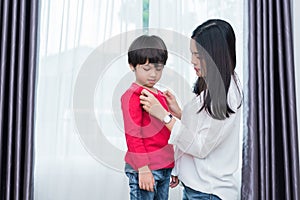 Young Asian mom dressed up son shirt for preparing go to school. Mother and son concept. Happy family and Home sweet home theme.