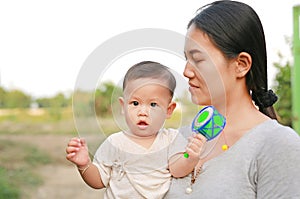 Young Asian mother carrying her baby boy and playing Pongapaeng toys Chinese Toy outdoors