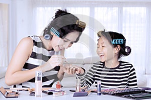 Young asian mother and daughter with hair curlers are doing nail polish at home