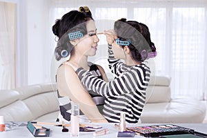 Young asian mother and daughter with hair curlers are shaping eye brows at home