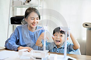 Young Asian mother is energy engineers enjoy looking at her son, spending time with little kid son playing with wind turbine at