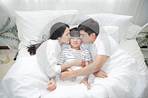 Young asian mother, father and boy sleeping in bed, mom and dad kiss on cheek of son,view from above