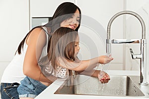 Young asian mother helping her daughter to wash hands